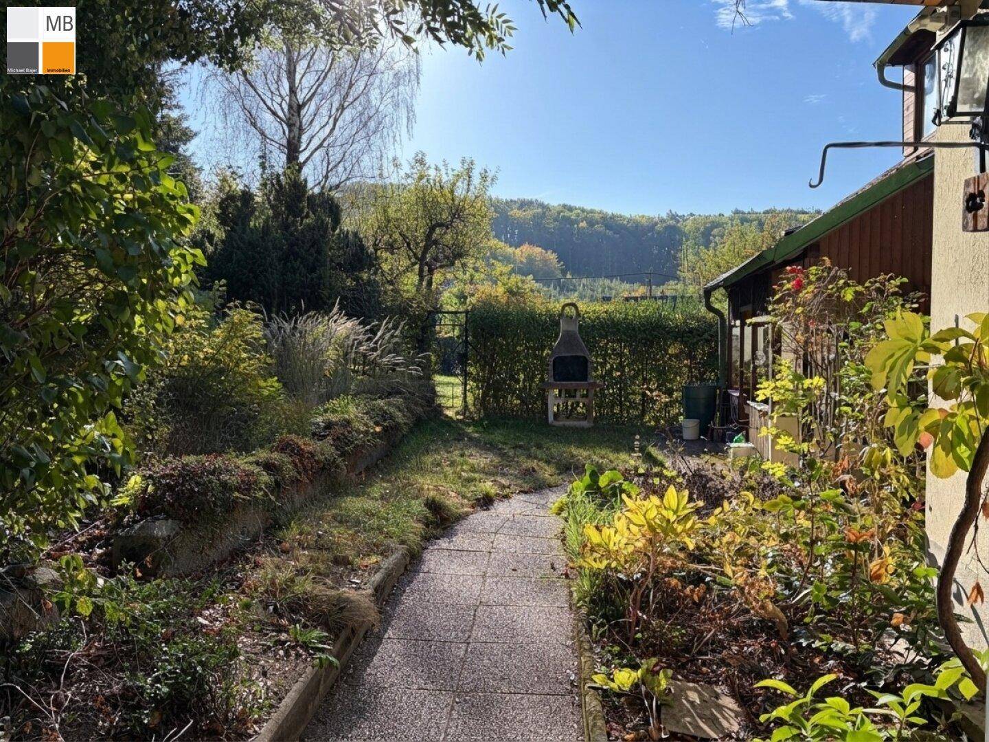 Idyllischer Gartenweg führt zu einem Grillplatz mit Blick auf die umliegende Hügellandschaft.