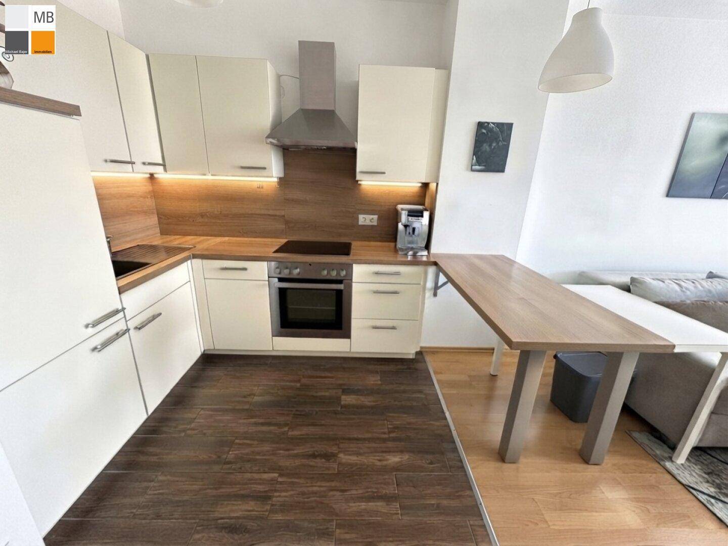 Moderne Küche mit hellen Schränken, Holzdetails und integriertem Essbereich in offenem Wohnkonzept.