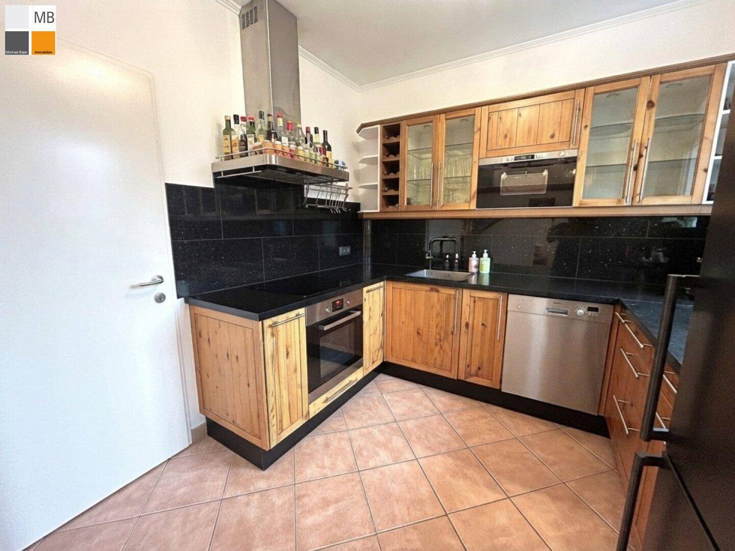 Funktionale Küche mit Holzschränken, schwarzen Arbeitsplatten und integrierten Geräten.