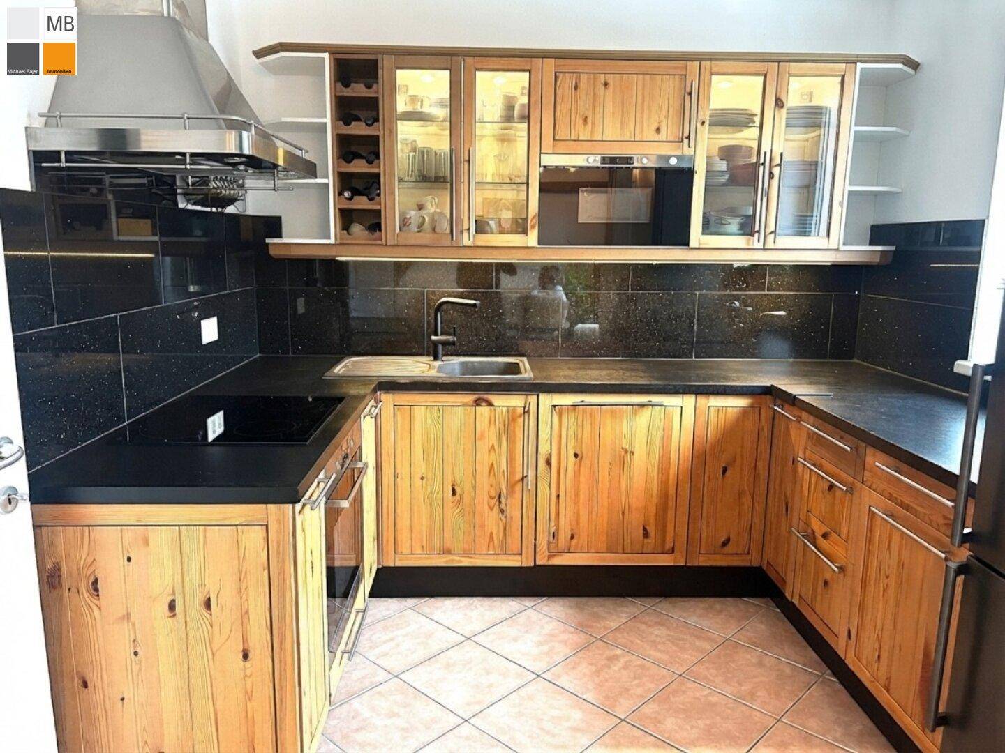 Voll ausgestattete Küche mit Holzschränken, dunklen Arbeitsflächen und modernen Geräten.