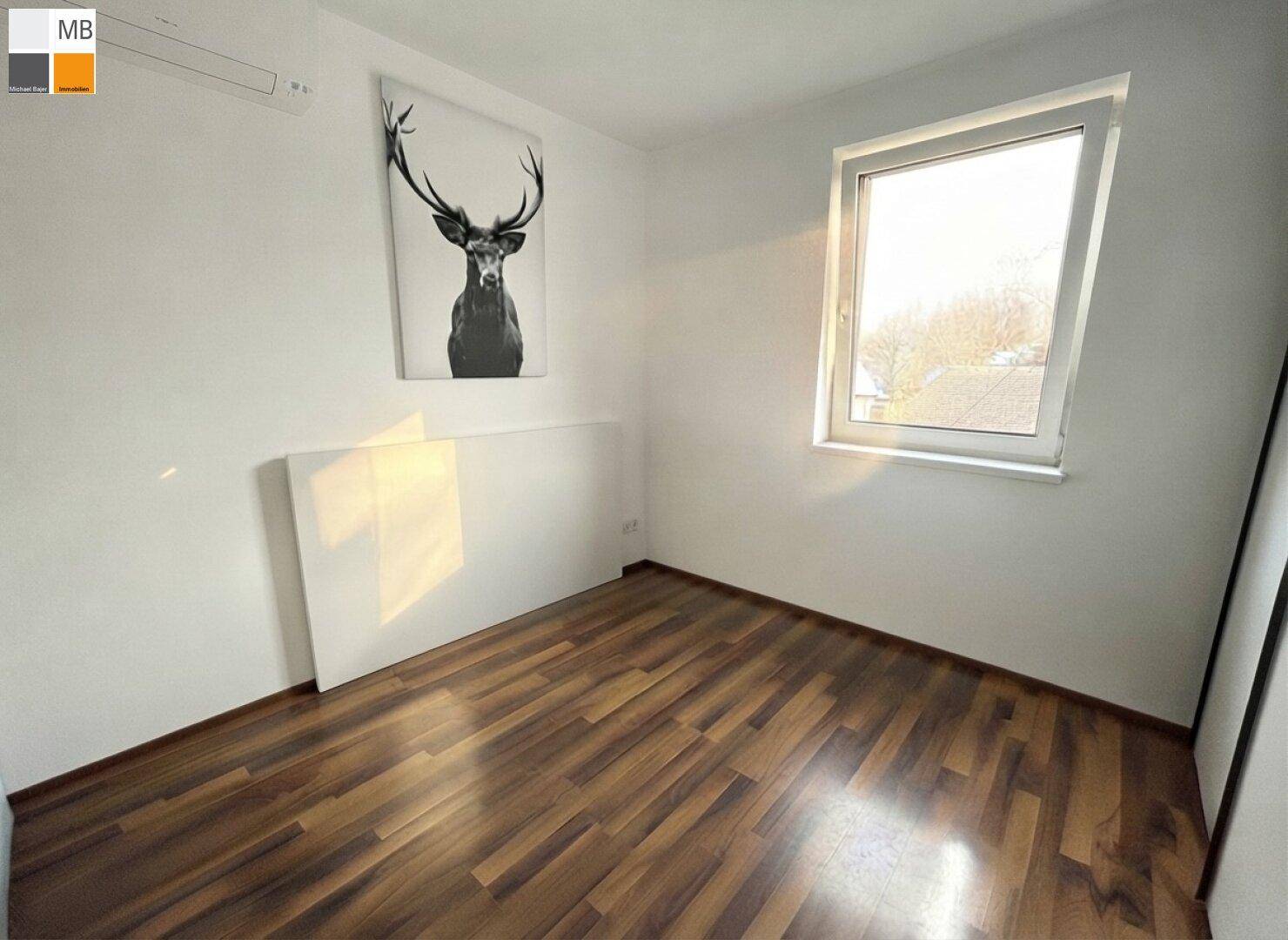Helles Schlafzimmer mit Holzboden und einem großen Fenster, das viel Tageslicht hereinlässt.