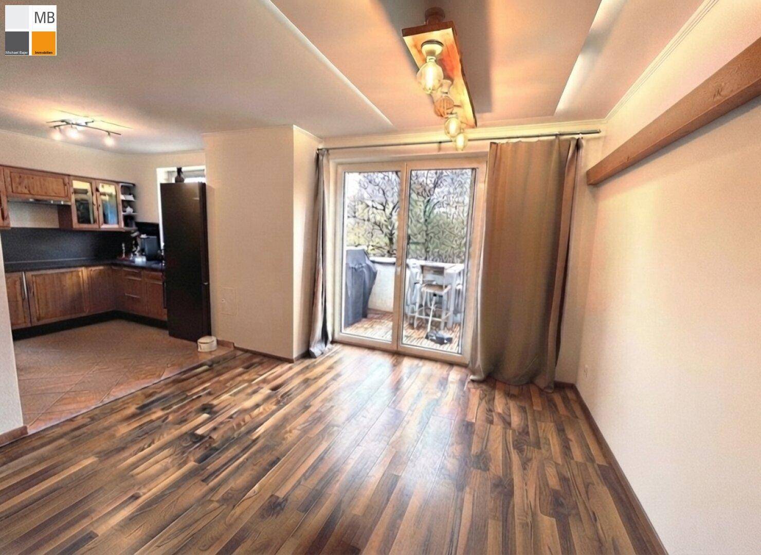 Heller Wohnbereich mit Holzboden und Zugang zum Balkon, angrenzend an eine Küche.