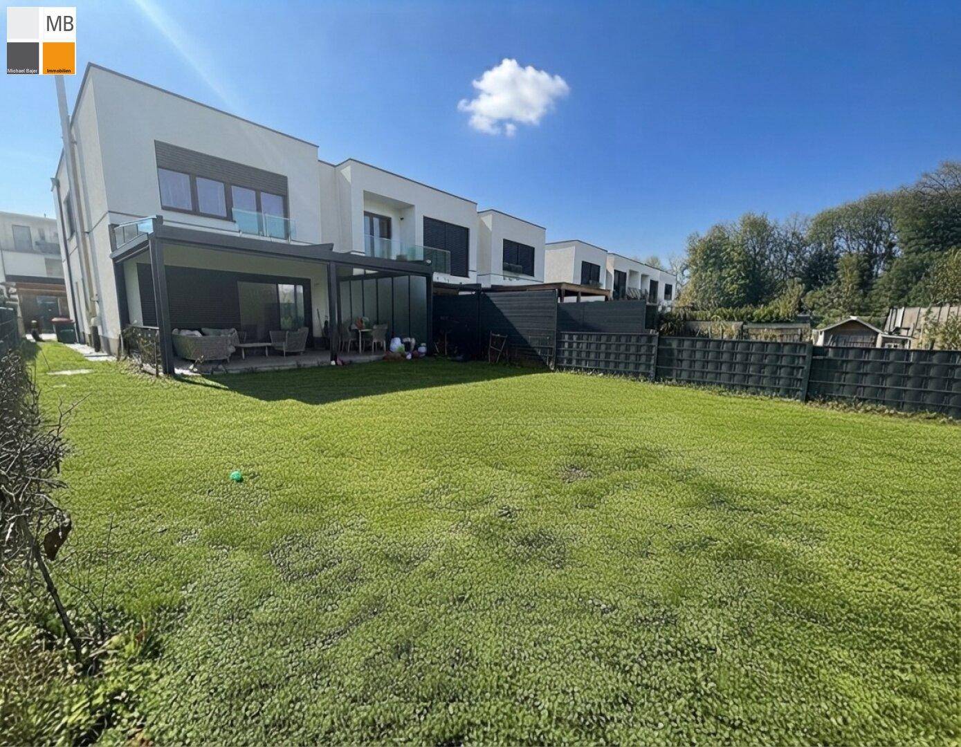 Moderner Neubau mit großem, gepflegtem Rasen und einer überdachten Terrasse im Hintergrund.