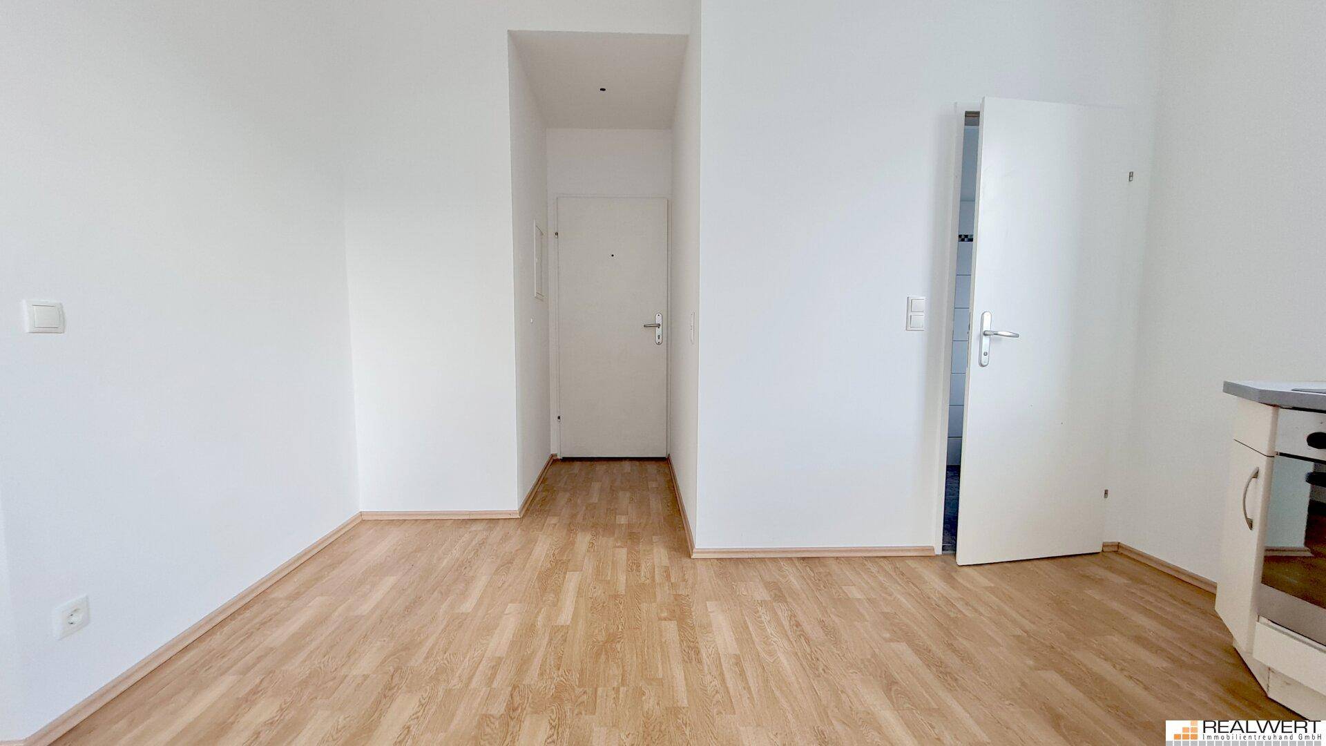 Leerer Raum mit Laminatboden, weiß gestrichenen Wänden und Zugang zu einem weiteren Zimmer.