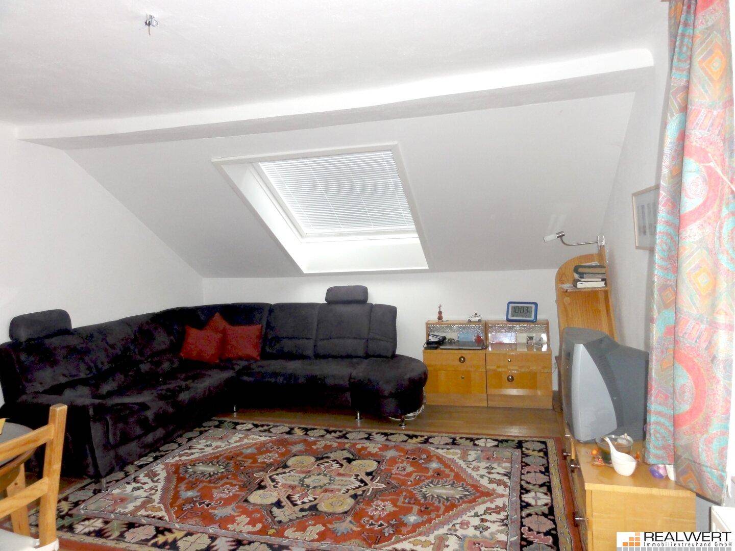 Gemütliches Wohnzimmer im Dachgeschoss mit Schrägdach, Sofa und Teppichboden.