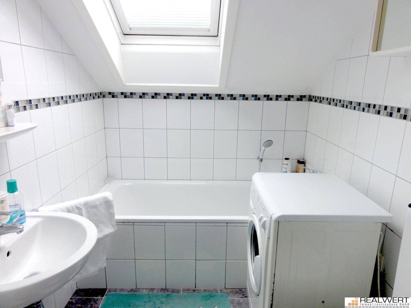 Gefliestes Badezimmer mit Badewanne, Waschbecken und Dachfenster für natürliches Licht.