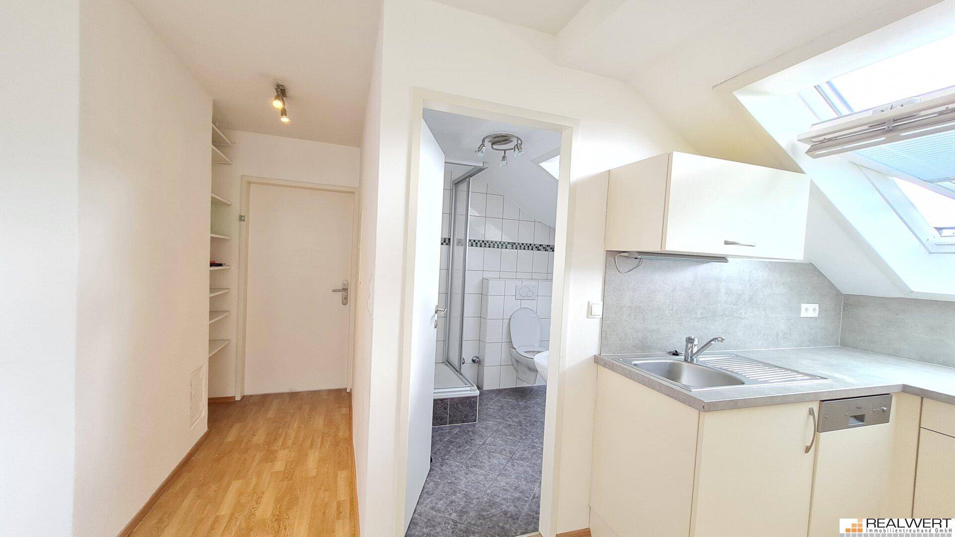 Kleine Küchenzeile mit Spüle und angrenzendem Badezimmer mit Dusche und WC.