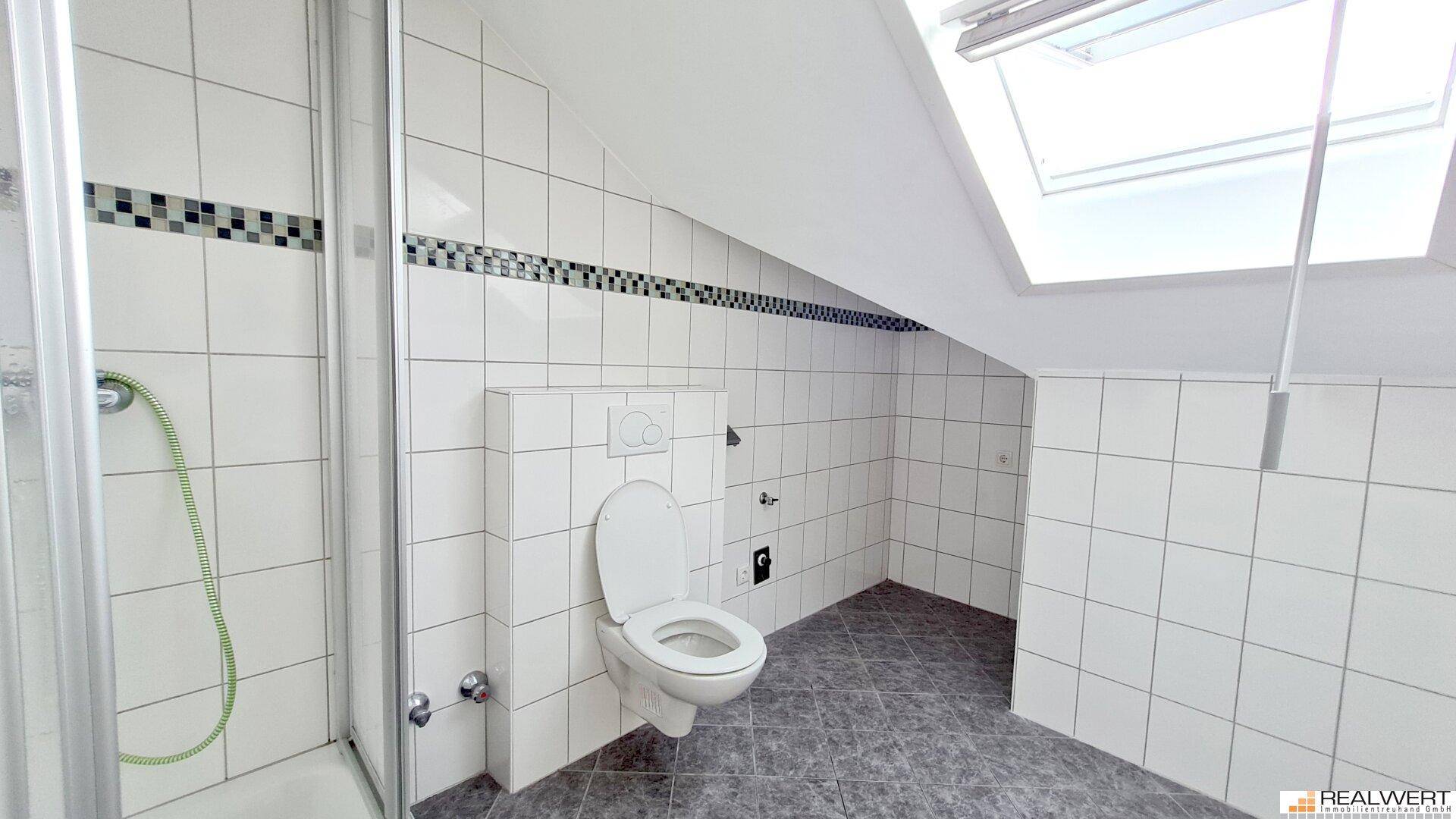 Helles Badezimmer im Dachgeschoss mit Dusche, WC und Dachfenster für Tageslicht.