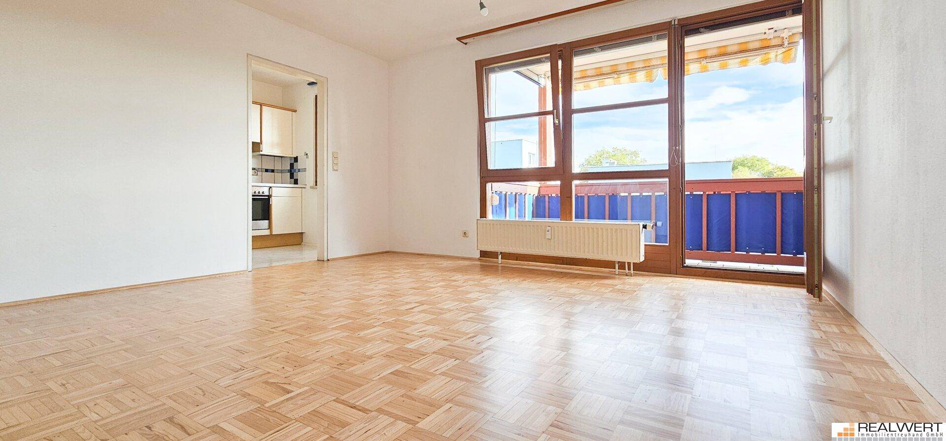Helles Wohnzimmer mit Laminatboden und großem Fenster mit Zugang zum Balkon.