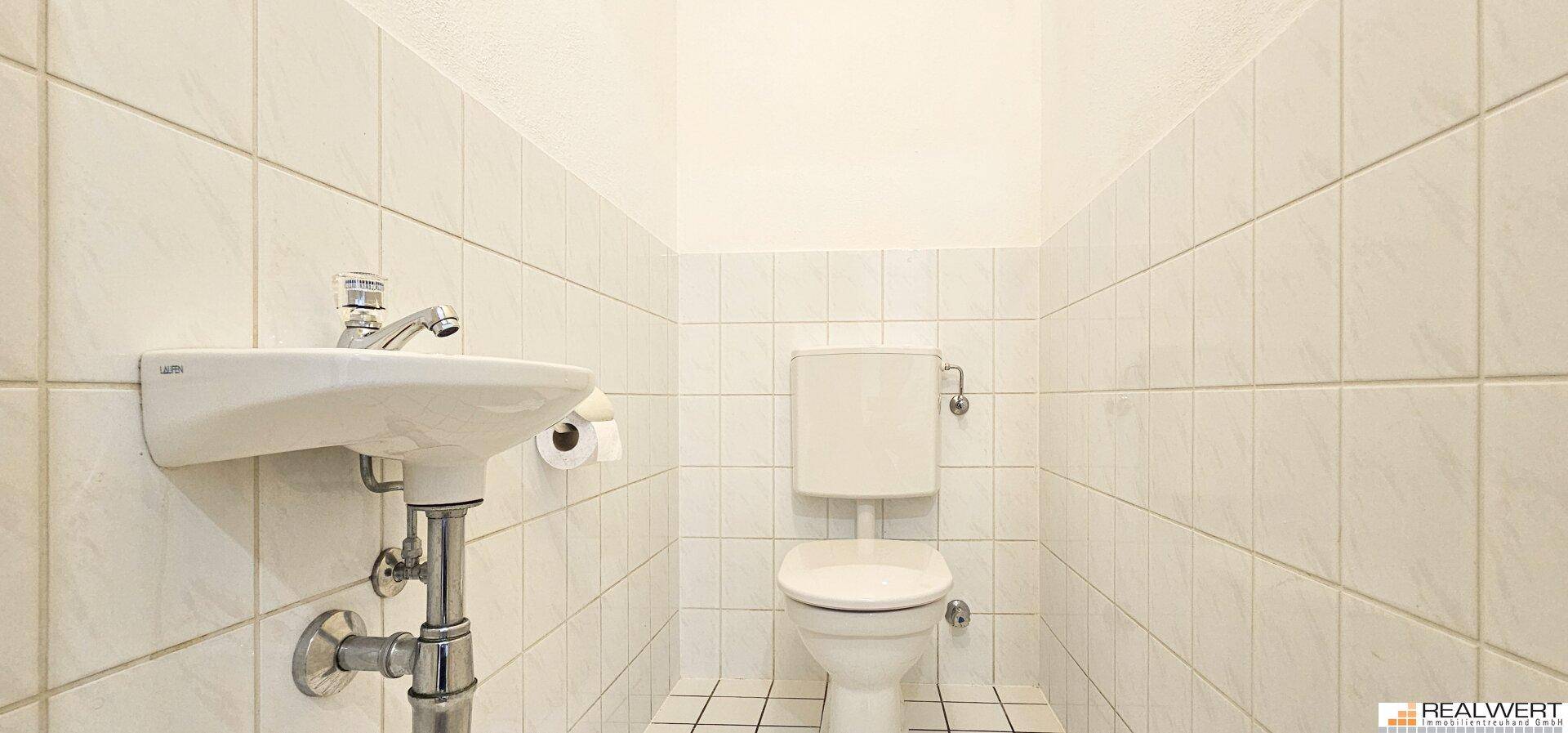 Kleines, hell gefliestes Gäste-WC mit Toilette und Handwaschbecken.