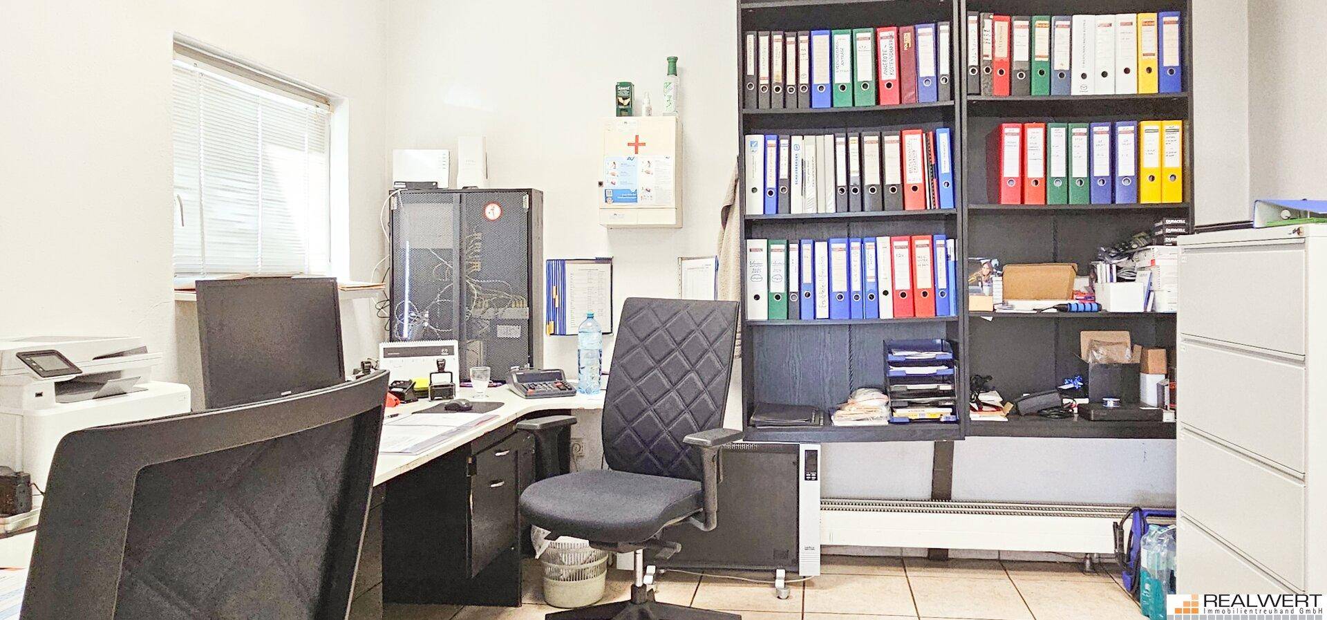 Funktionales Büro mit Schreibtisch, Bürostuhl, Regalen voller Aktenordner und einem Fenster.