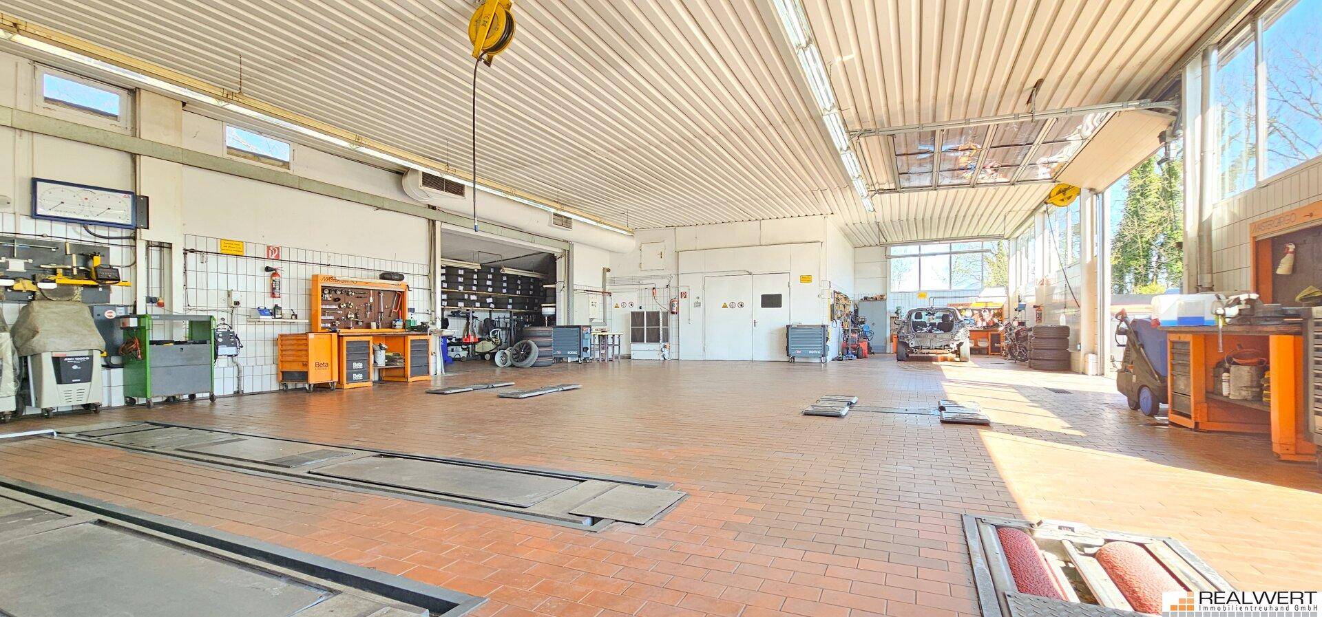 Geräumige Autowerkstatt mit Hebebühnen, Werkzeugen und Tageslicht durch große Fenster.