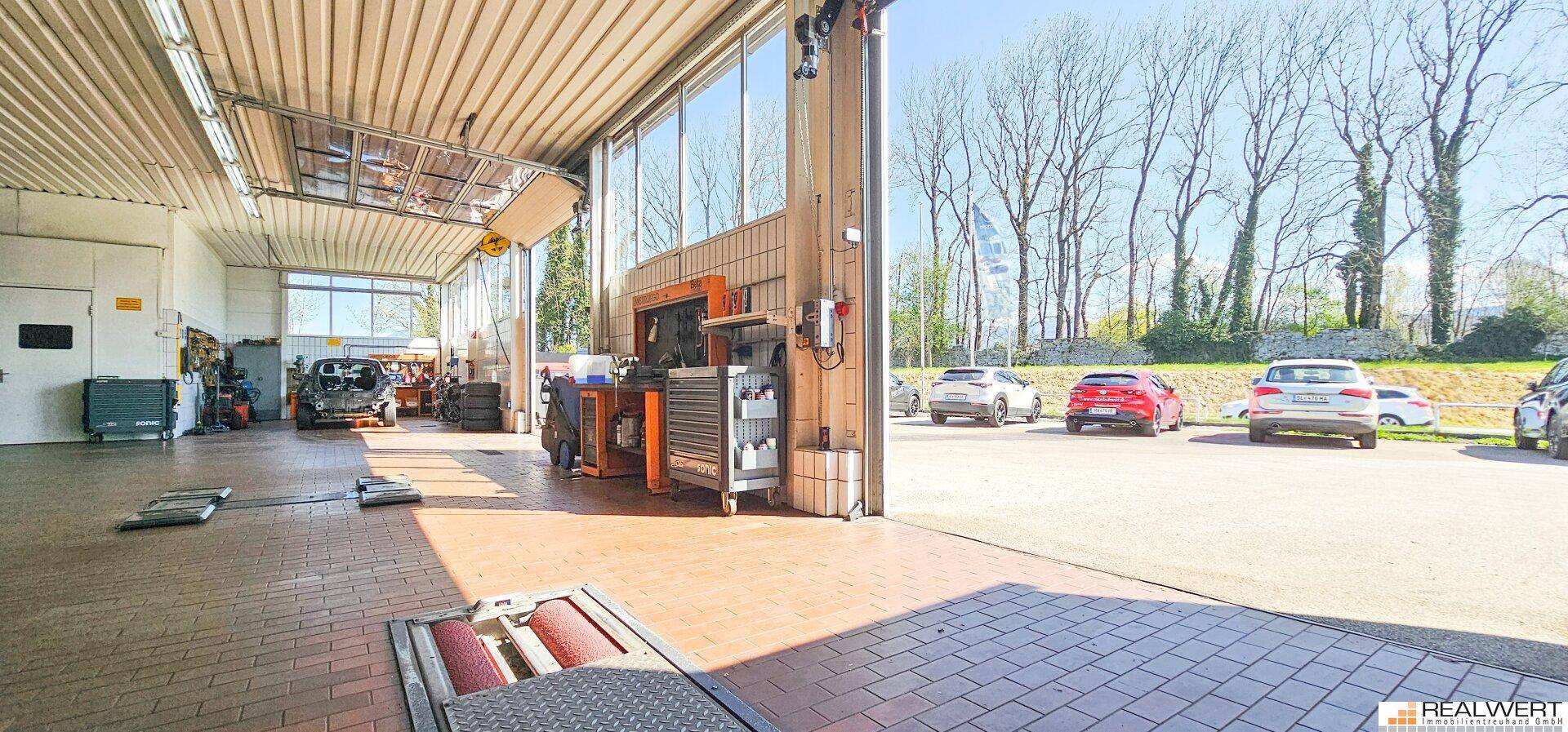 Werkstattbereich mit geöffnetem Garagentor, das den Blick auf den Außenbereich und geparkte Autos freigibt.