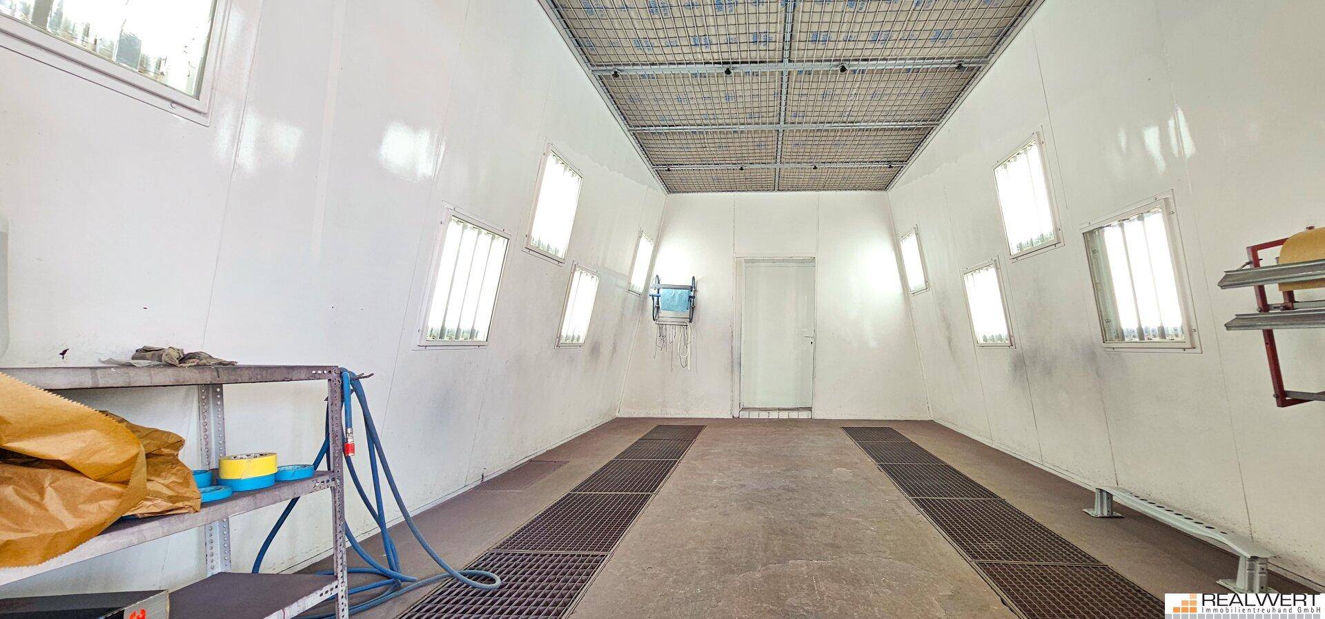 Innenansicht einer Lackierkabine mit Gitterrosten im Boden und mehreren Fenstern für Belüftung und Licht.