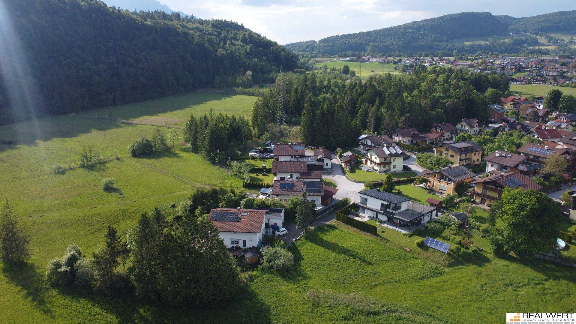Panoramablick aus der Luft auf die Wohnsiedlung, umgeben von üppiger Natur und majestätischen Bergen.