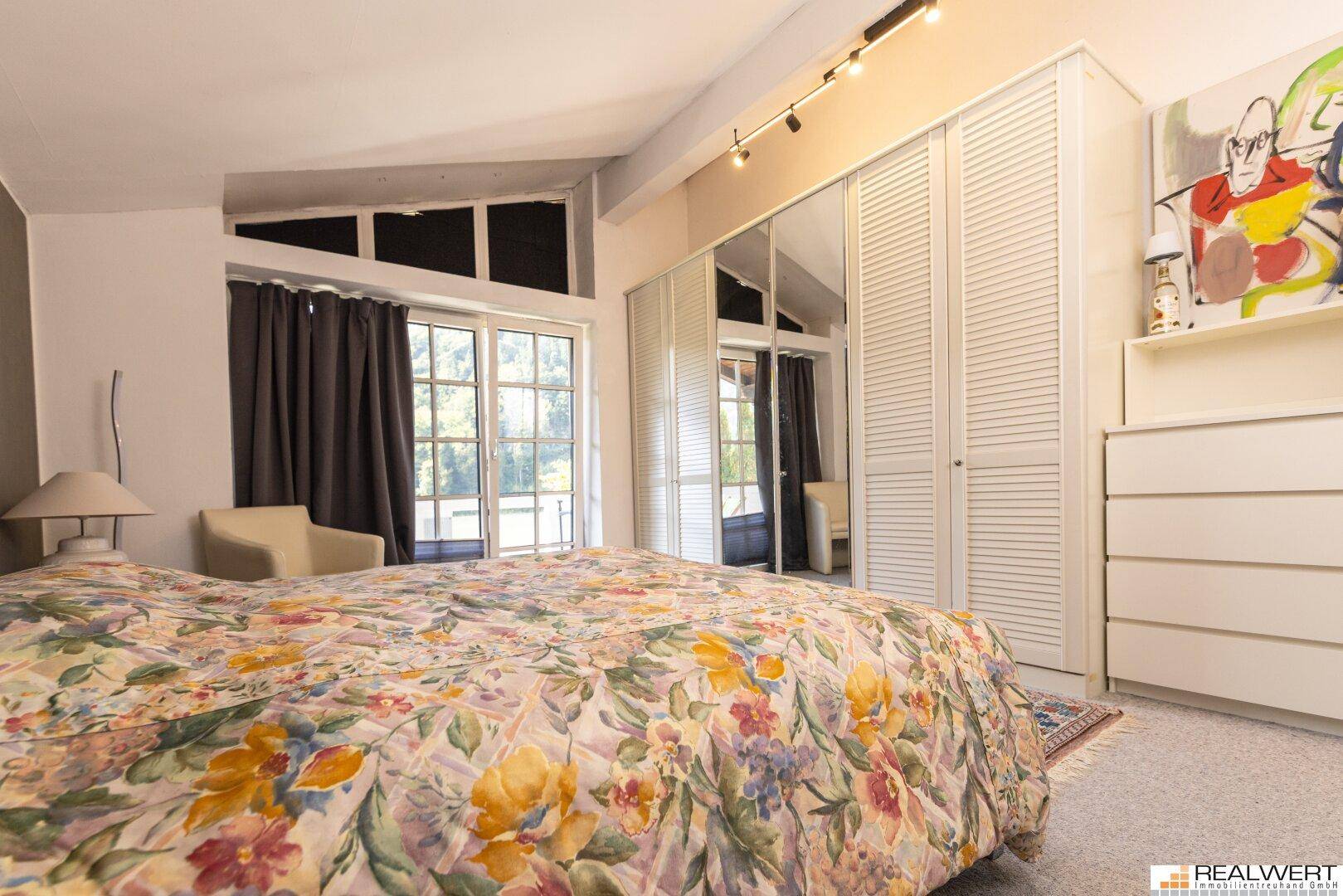 Schlafzimmer mit großem Bett, Spiegelschränken und Zugang zu einem Außenbereich, unter Dachschräge.