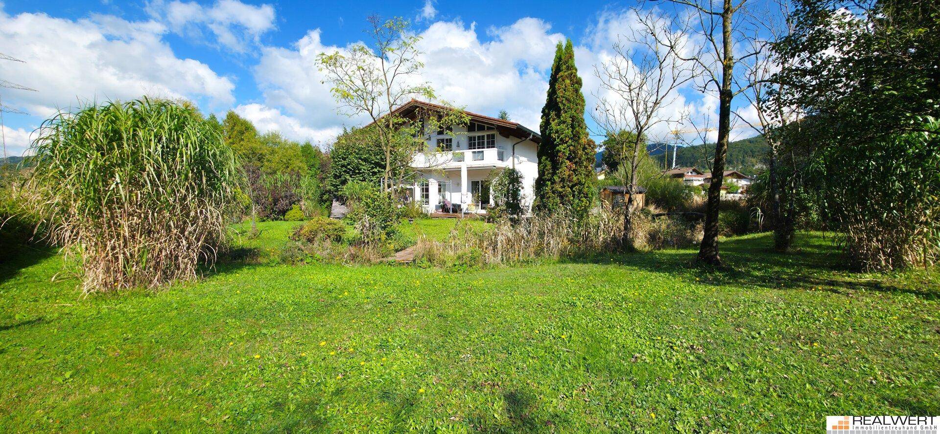 Weitläufiger grüner Garten mit Rasenfläche und Bäumen, der zum weißen Wohnhaus führt.