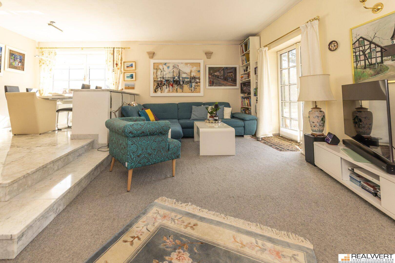 Gemütliches Wohnzimmer mit Teppichboden, blauer Couch und Zugang zu einem Außenbereich.