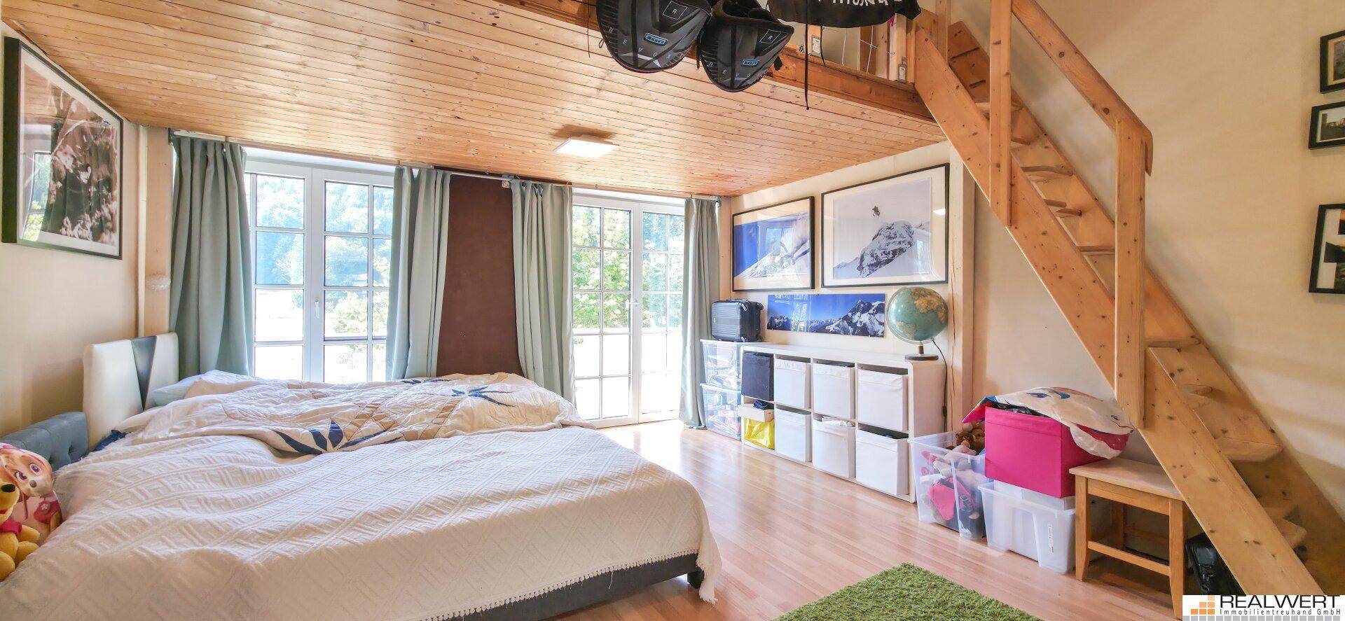 Schlafzimmer mit Holzdecke, Holzboden und einer Holztreppe, die zu einem erhöhten Bereich führt.