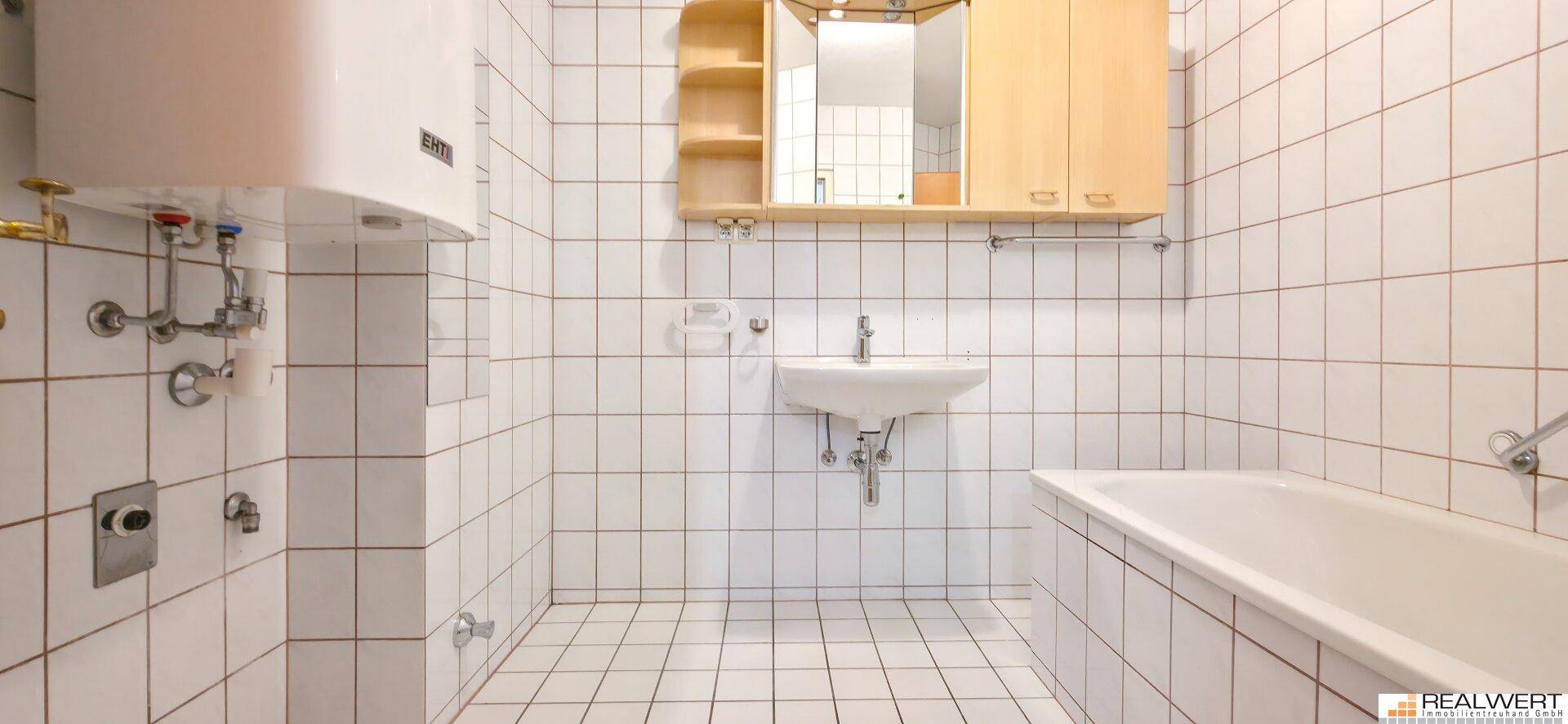 Gefliestes Badezimmer mit Badewanne, Waschbecken und Spiegelschrank.