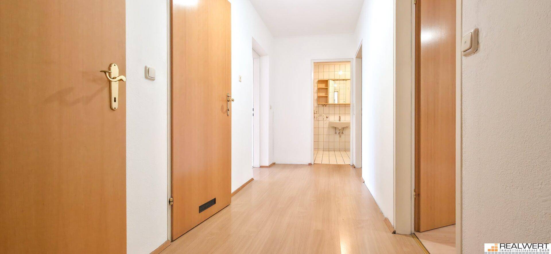 Heller Flur mit Laminatboden und mehreren Holztüren, der zu einem Badezimmer führt.