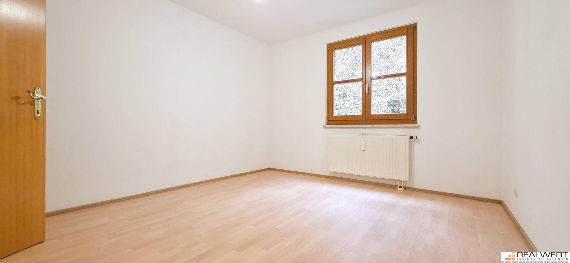 Helles Schlafzimmer mit Laminatboden und einem Fenster, das viel Tageslicht hereinlässt.