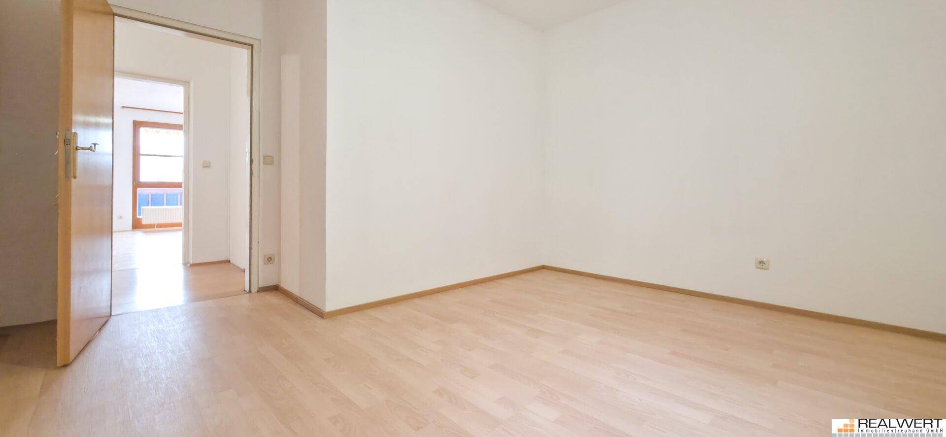 Leeres Schlafzimmer mit hellem Laminatboden und Zugang zu einem weiteren Raum.
