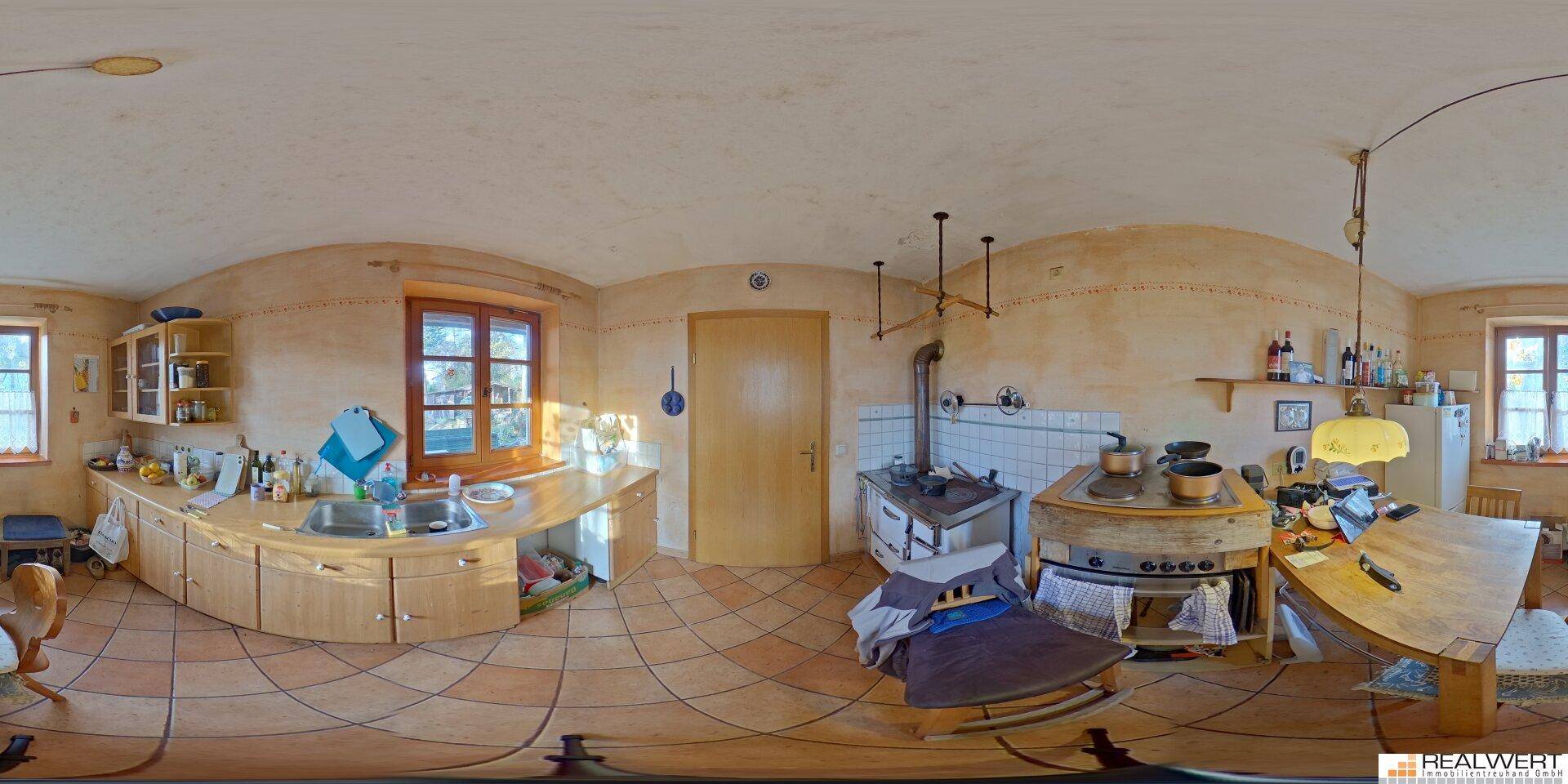 Panoramaansicht einer rustikalen Küche mit Holzmöbeln, Terrakottafliesen und einem traditionellen Ofen.