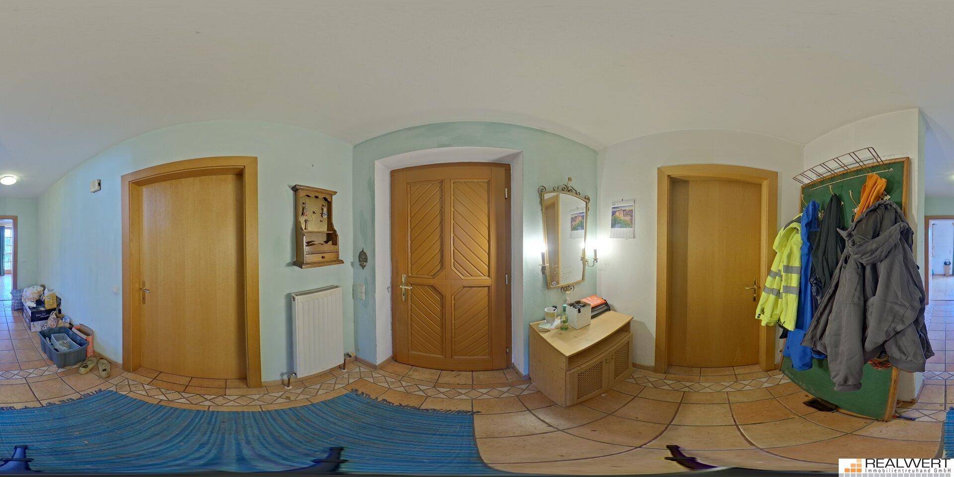 Panoramaansicht des Eingangsbereichs mit Holztür, Fliesenboden und Garderobe.
