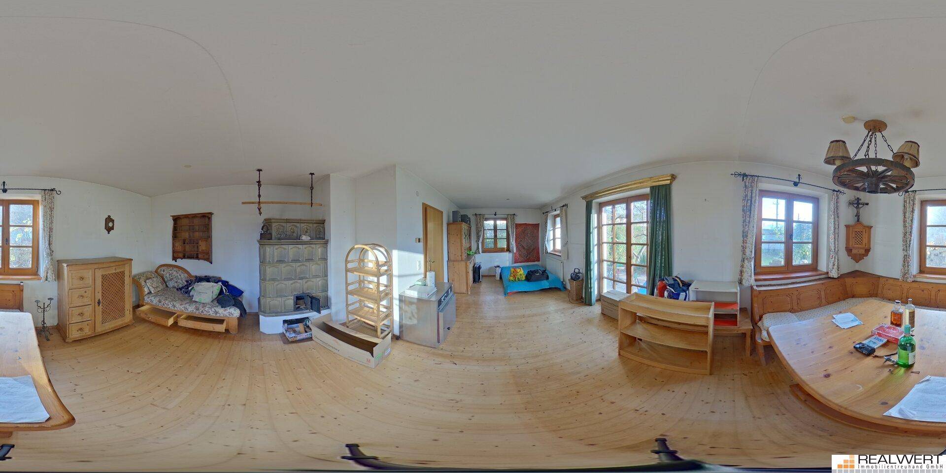 Panoramaansicht eines großen Wohnbereichs mit Holzboden, Kachelofen und traditionellen Holzmöbeln.