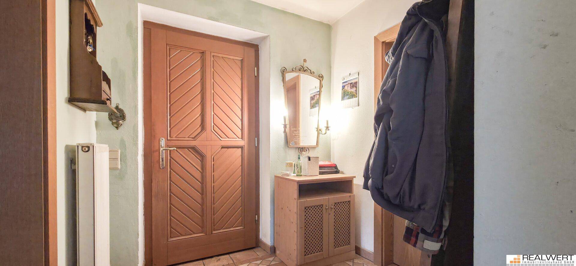 Rustikaler Eingangsbereich mit Holztür, Fliesenboden und einem kleinen Holzschrank mit Spiegel.