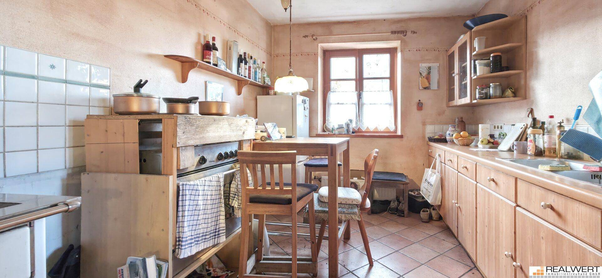 Gemütliche Küche im Landhausstil mit Holzmöbeln, Terrakottafliesen und einem Esstisch am Fenster.