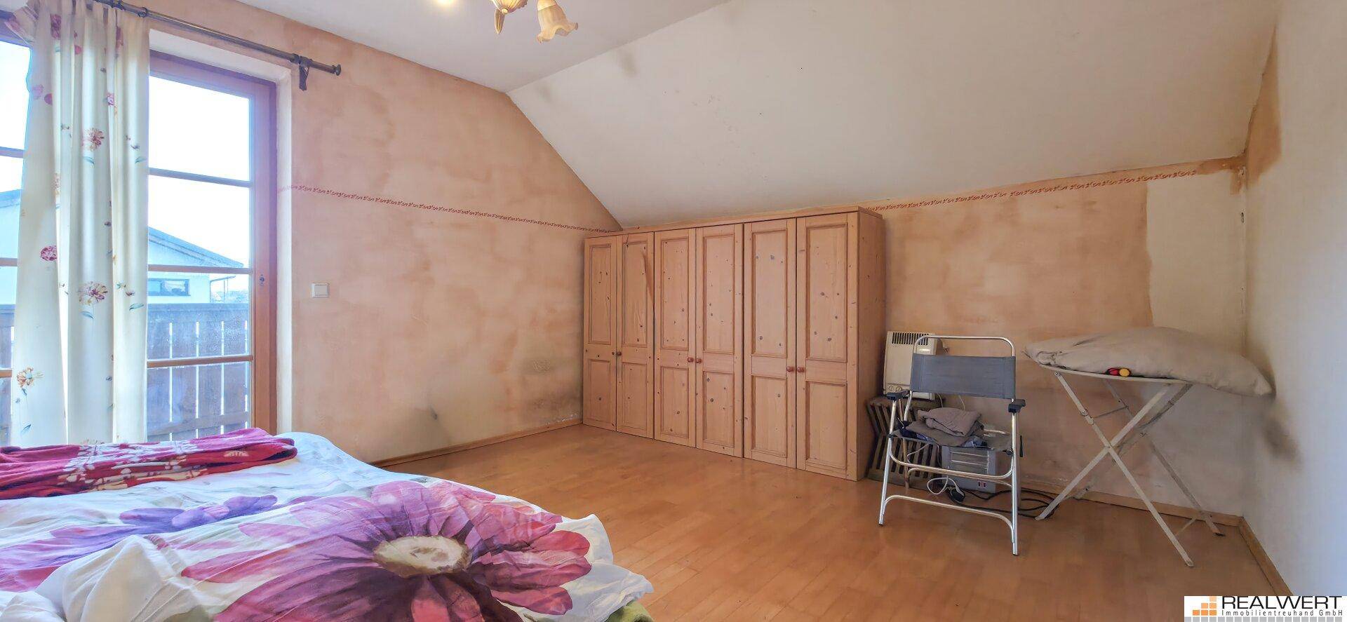 Schlafzimmer im Dachgeschoss mit Holzboden, Einbauschränken und Zugang zu einem kleinen Balkon.