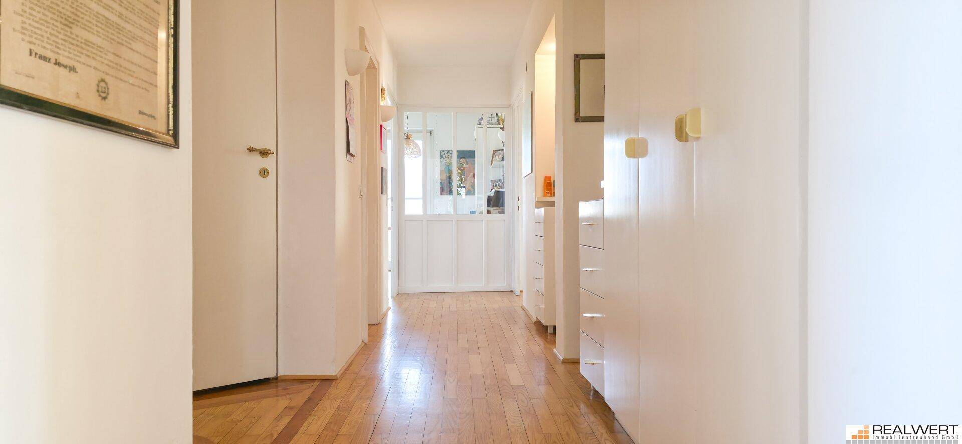 Langer Flur mit Holzparkettboden, weißen Wänden und Einbauschränken, der zu einem weiteren Bereich führt.