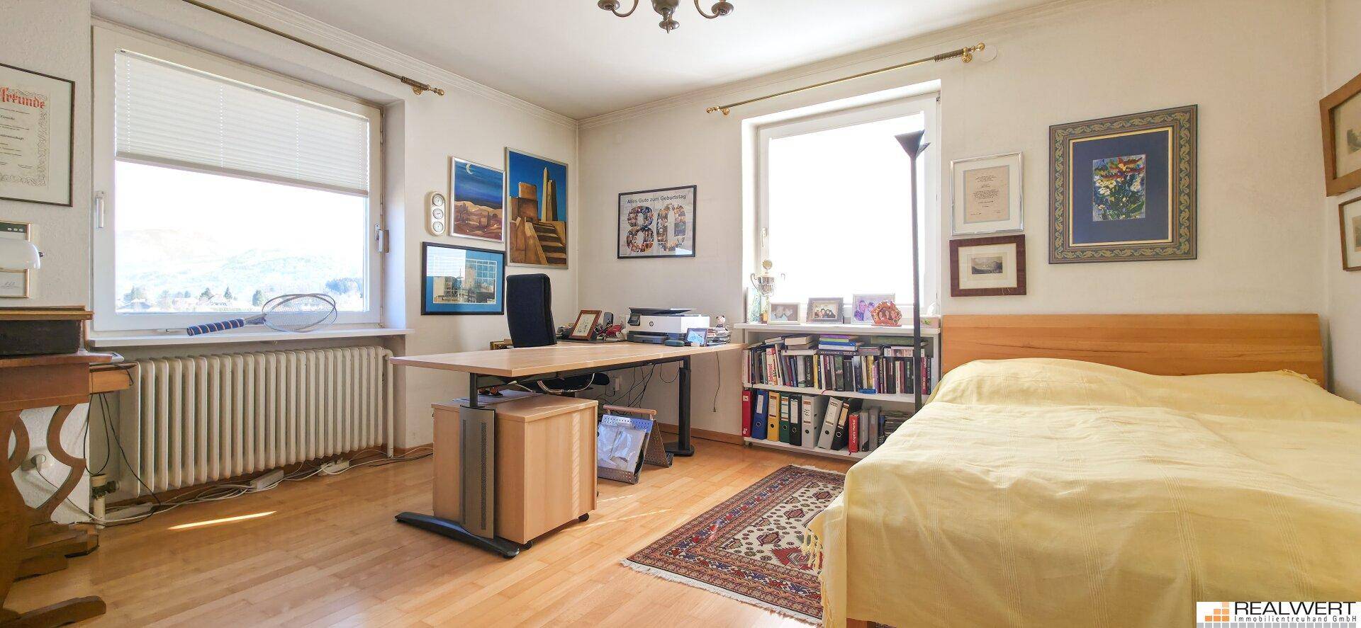 Helles Schlafzimmer mit Holzboden, großem Fenster, Bett und einem Arbeitsbereich mit Schreibtisch.