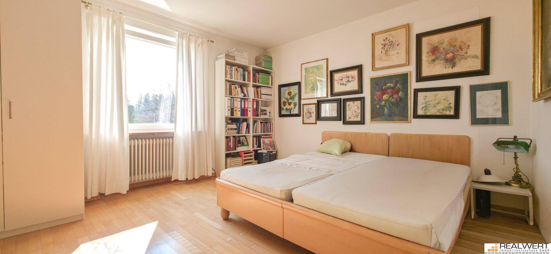 Gemütliches Schlafzimmer mit Holzboden, großem Fenster, Doppelbett und Bücherregal.