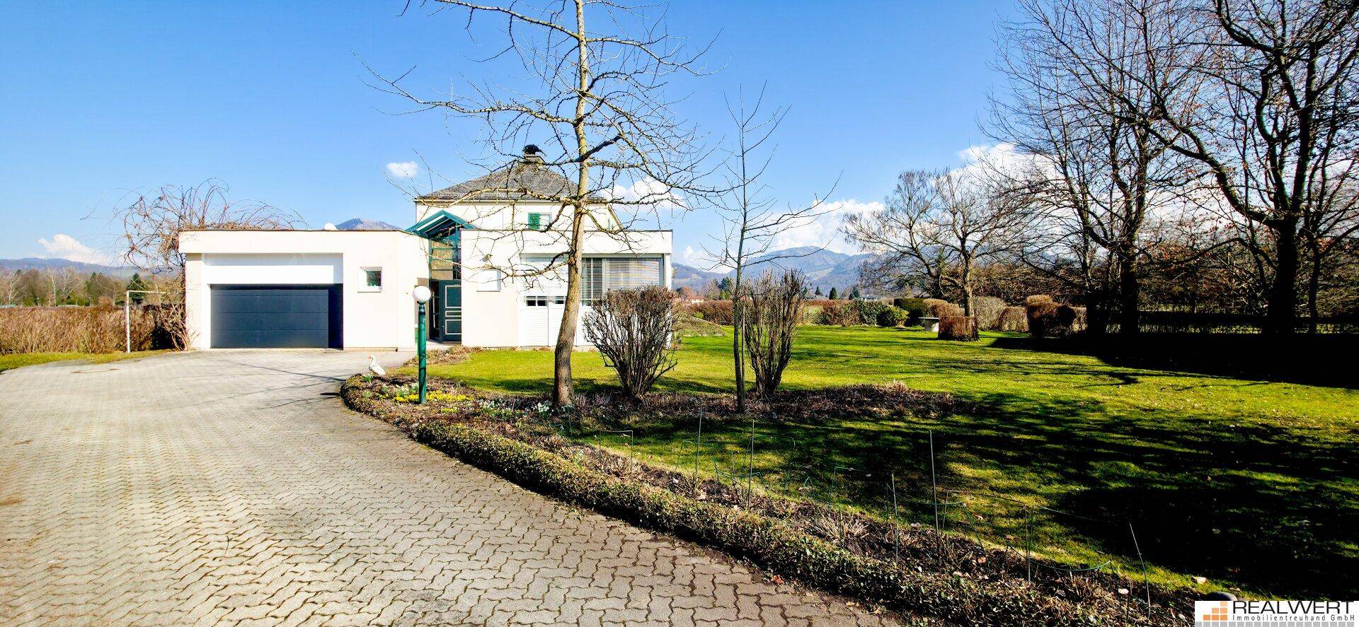 Einfamilienhaus mit Garage, gepflasterter Auffahrt und weitläufigem Garten unter blauem Himmel.