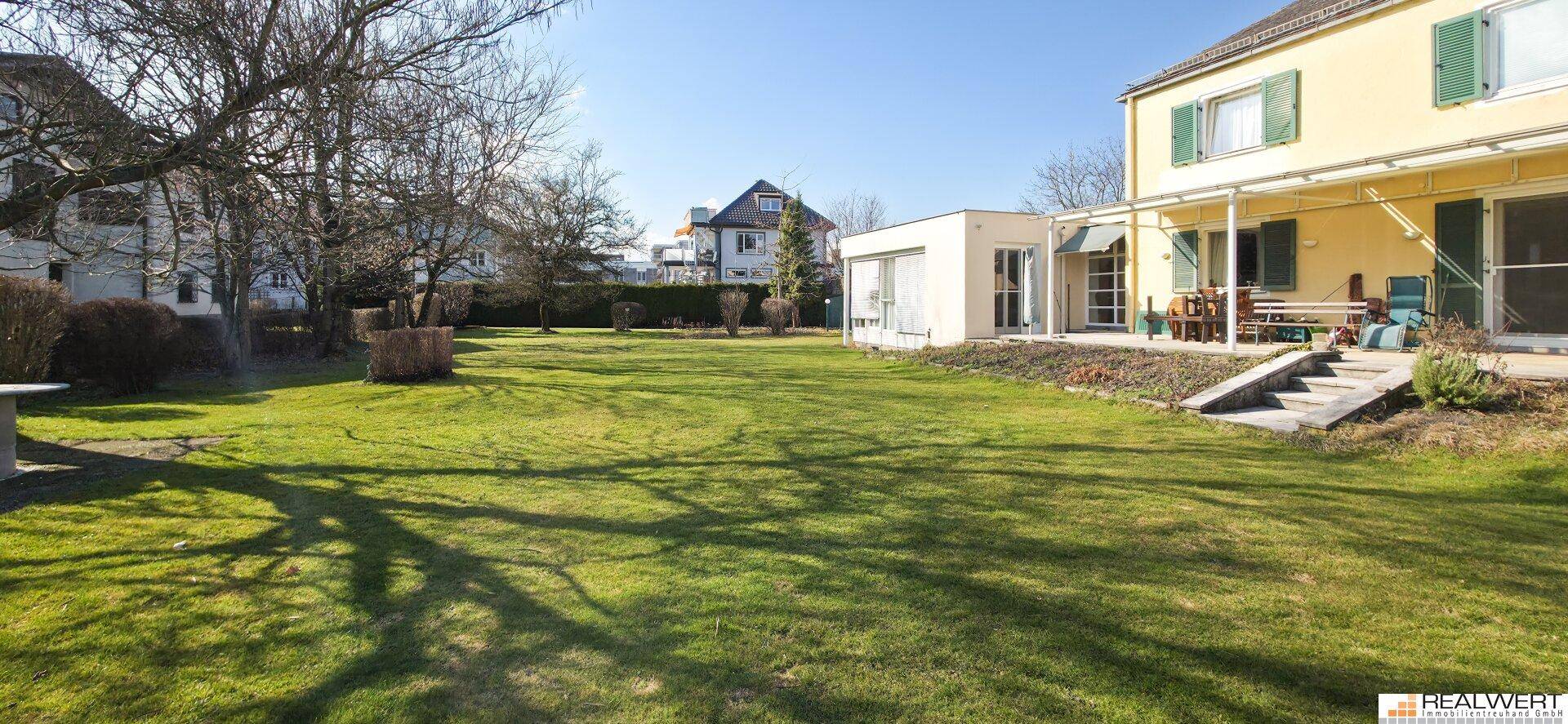 Großer, gepflegter Garten mit Rasenfläche und Terrasse am Haus, ideal für Entspannung im Freien.