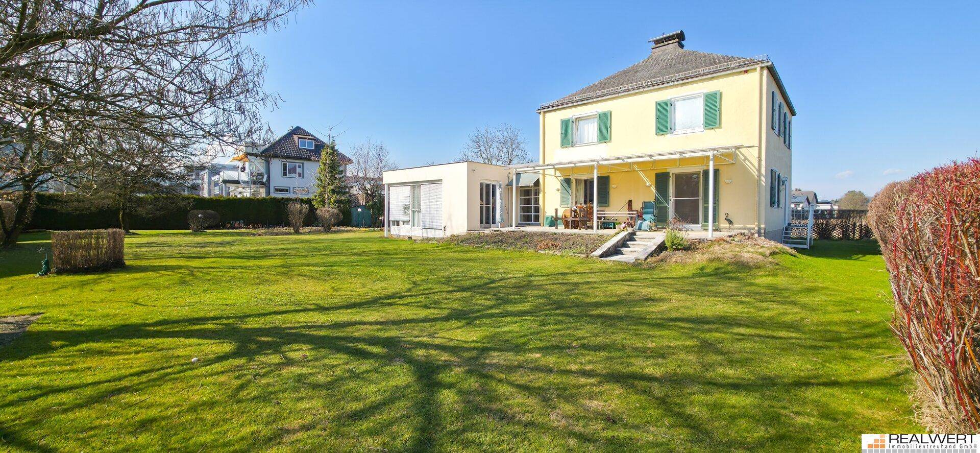 Gepflegter Garten mit Rasenfläche und Blick auf das gelbe Einfamilienhaus mit Terrasse.