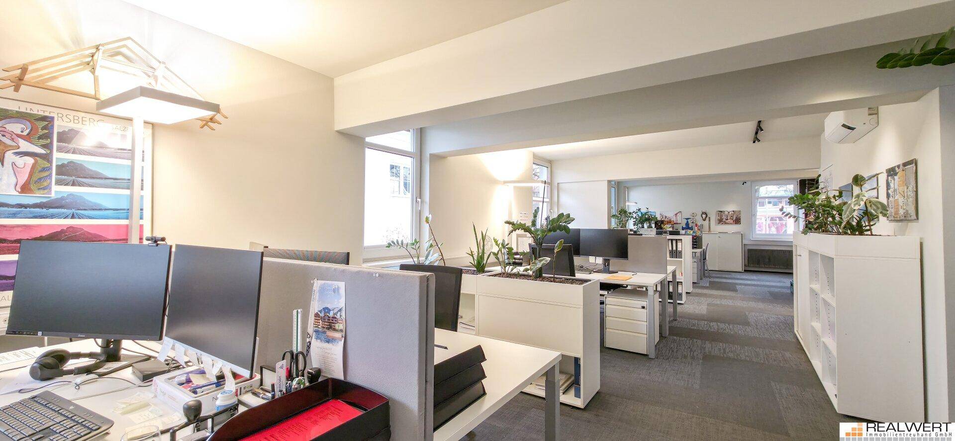 Geräumiges Büro mit mehreren Arbeitsstationen, viel Tageslicht und modernen Büromöbeln.