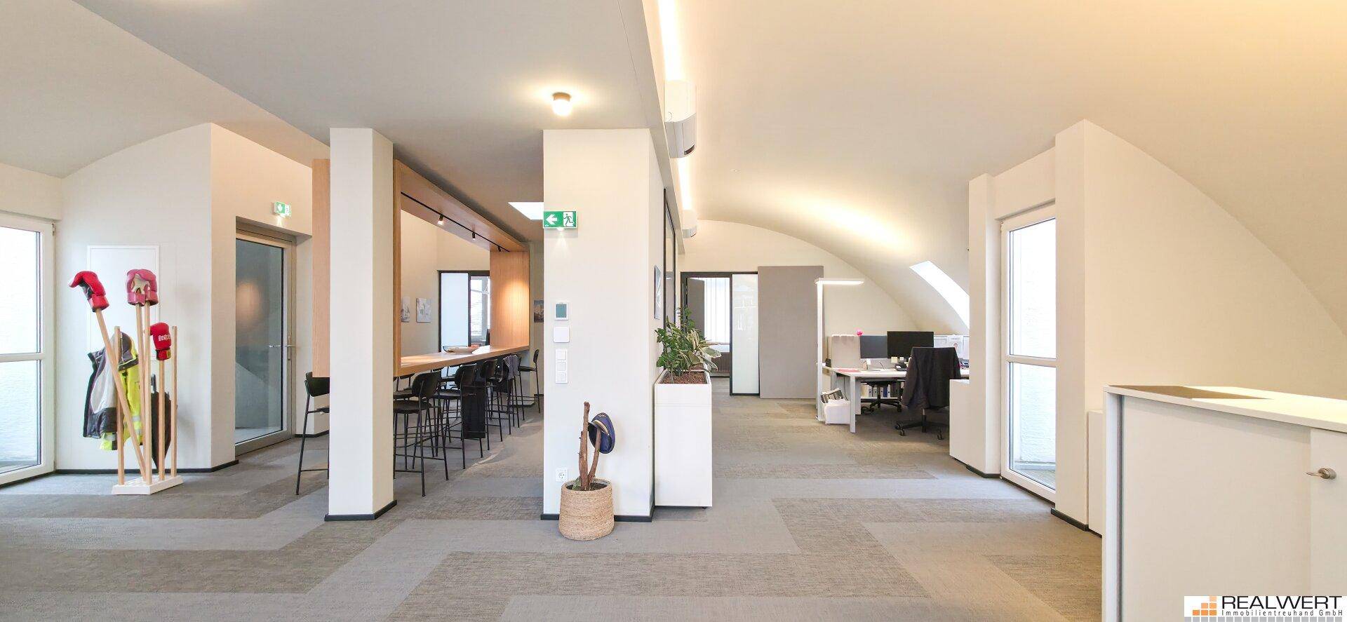 Weitläufiges Dachgeschossbüro mit geschwungenen Decken, großen Fenstern und modernen Möbeln.