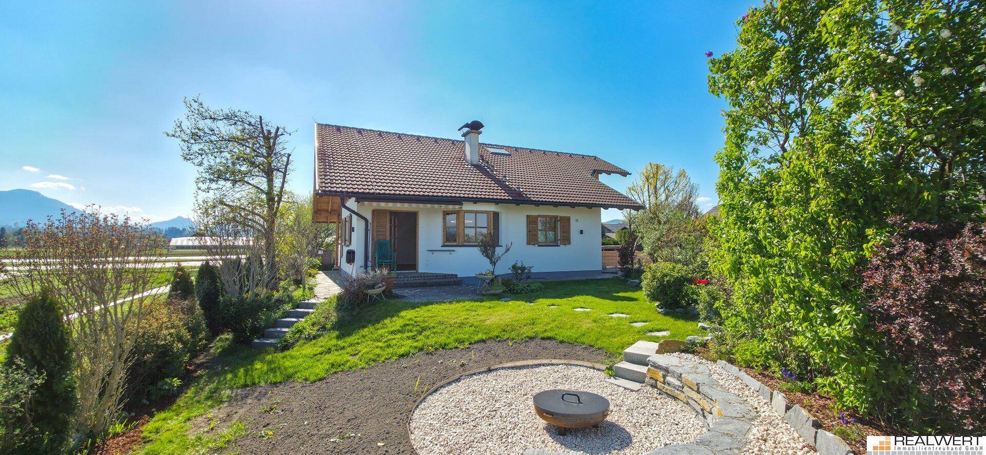 Großer Garten mit Rasenfläche, Feuerstelle und Blick auf das Haus und die Berge.