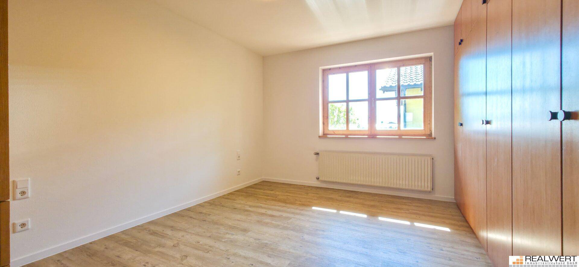 Schlafzimmer mit Holzboden, großem Fenster und praktischen Einbauschränken für Stauraum.