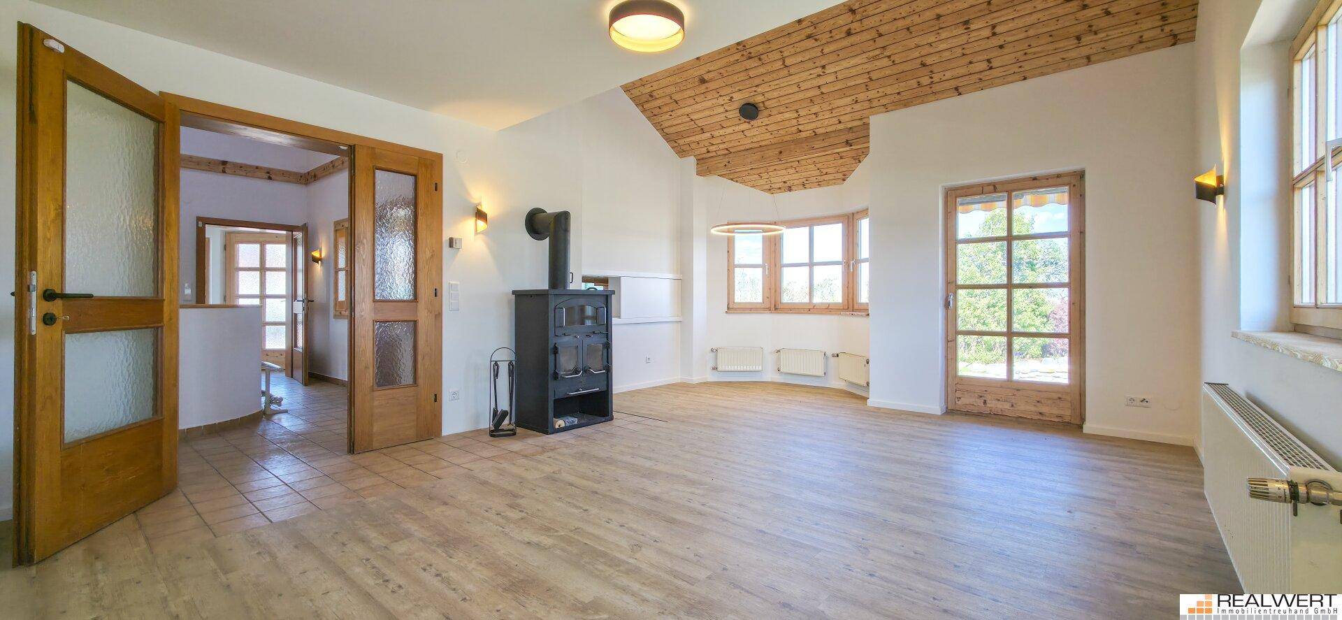 Geräumiges Wohnzimmer mit Holzboden, einem Kaminofen und Zugang zum Außenbereich durch eine Glastür.