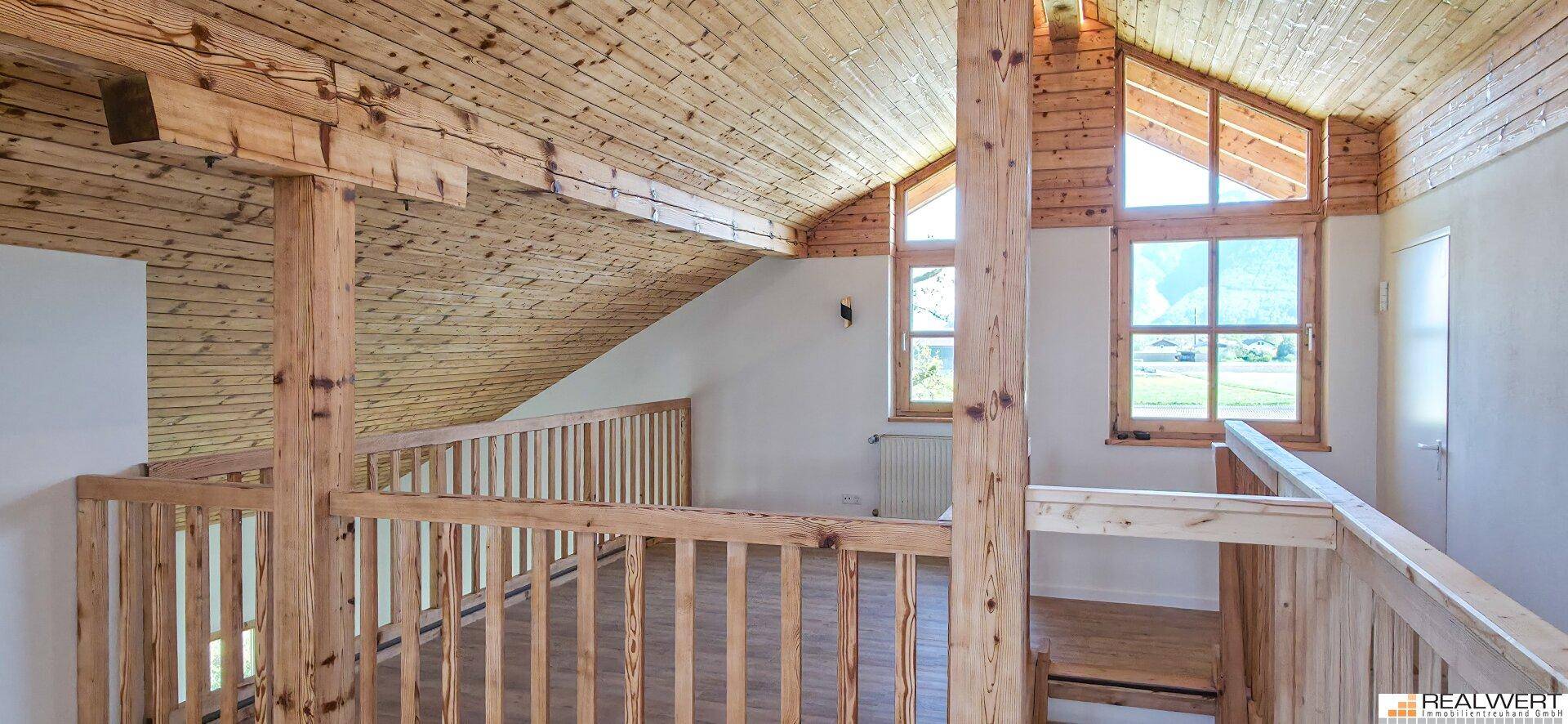 Obere Galerie mit Holzboden und -geländer, die einen offenen Blick in den darunterliegenden Bereich bietet.