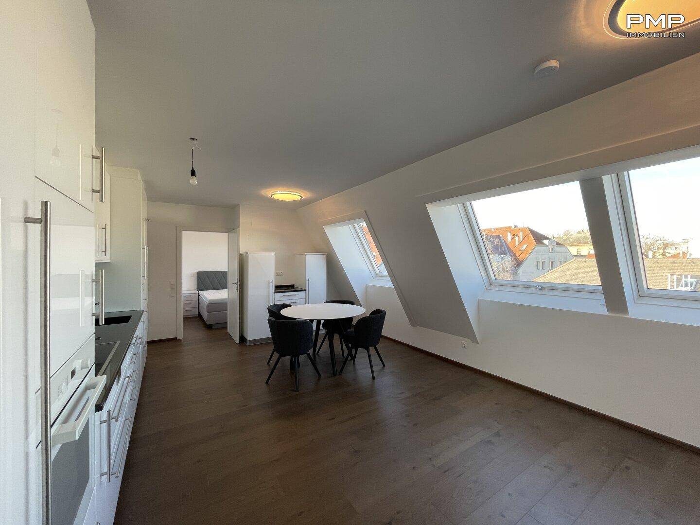 Offener Wohnbereich mit moderner Küche, Essplatz und Blick auf die Stadt durch Dachfenster.