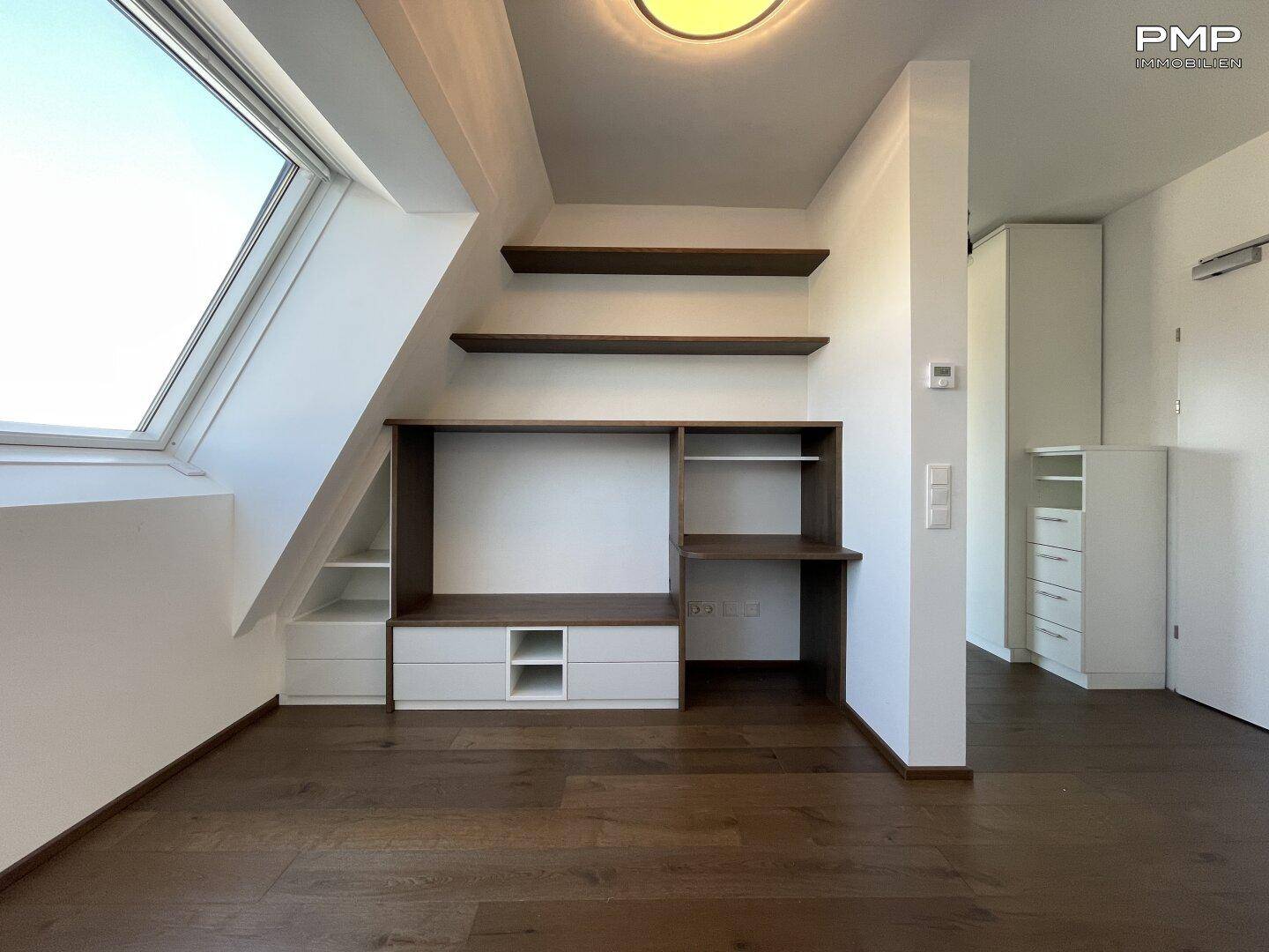 Maßgefertigte Einbaumöbel mit Schreibtisch und Regalen unter einem großen Dachfenster.