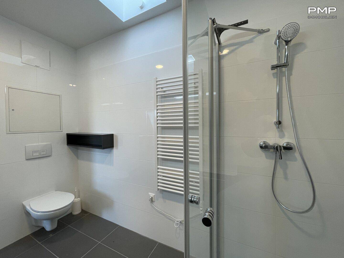 Badezimmer mit wandhängendem WC, Duschbereich und beheiztem Handtuchhalter.