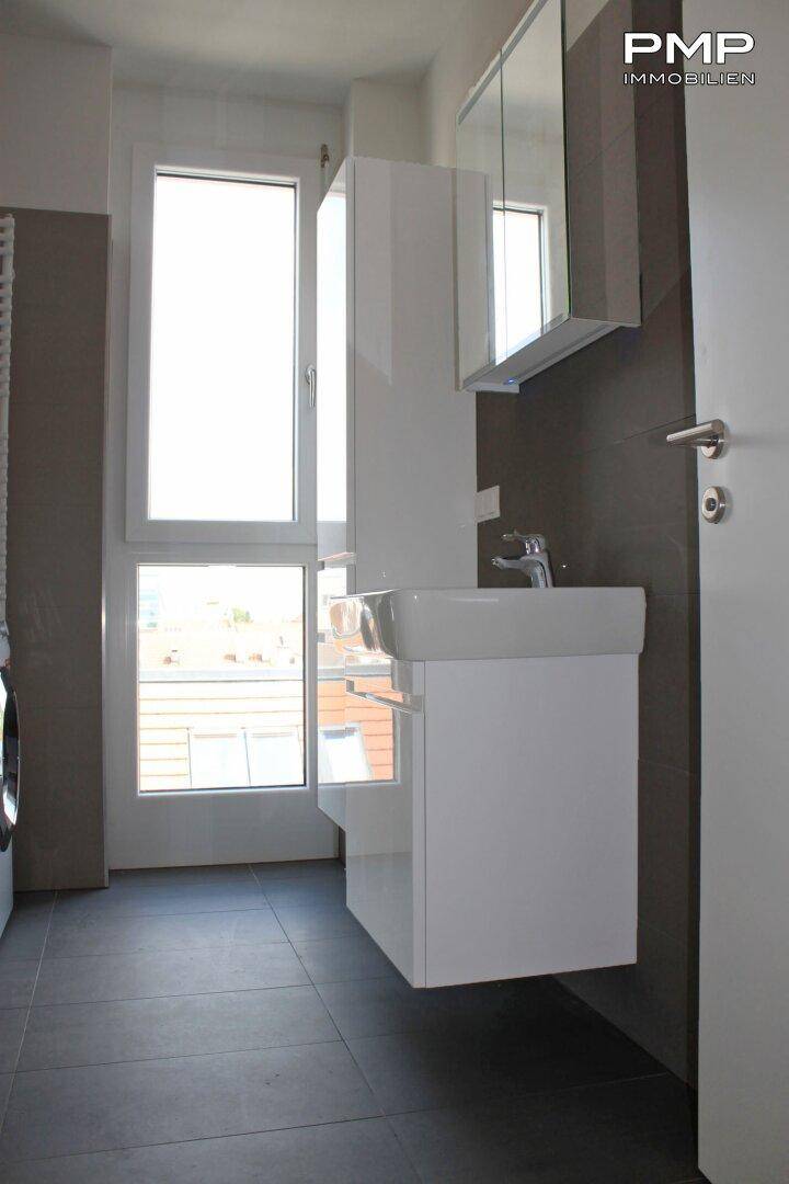 Modernes Badezimmer mit Waschbecken, Spiegelschrank und großem Fenster für Tageslicht.