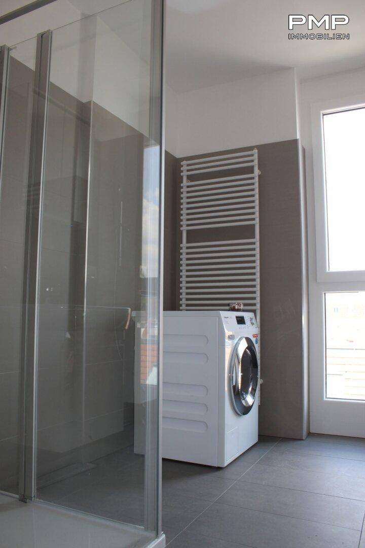 Badezimmer mit Duschkabine, Waschmaschine und beheiztem Handtuchhalter.